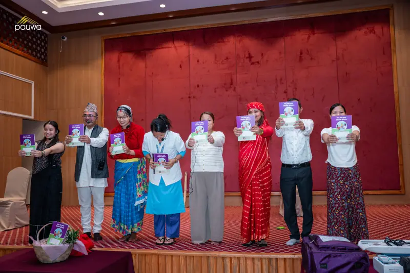Participants on stage holding up booklets at an indoor programme.
